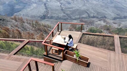 woman in glasses working with laptop on cafe balcony with view of Mount Bromo in Indonesia. outdoor working and remote working concept.