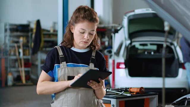 Portrait of smiling mechanic in garage workspace using tablet to order new parts for car after finding damages during annual checkup. Cheerful specialist looking online for automotive components