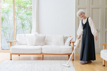 リビングを掃除するシニア女性 © taka