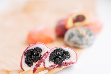 Half colored mochi with berry filling on a wooden board on a white background.