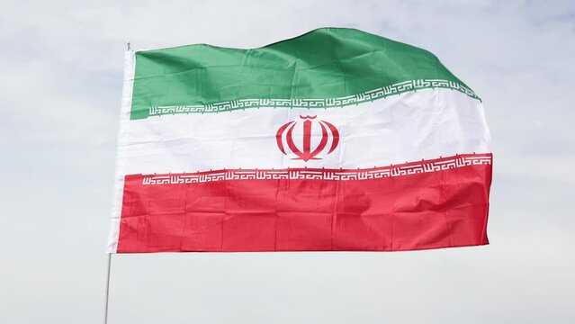 Large flag of Iran fixed on metal stick waving against background of clear sky during daytime 