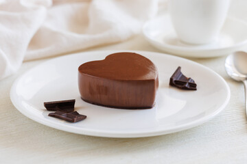 Valentine s day dessert, delicious dark chocolate mousse heart-shaped on white plate with spoon, cup of tea or coffee and napkin. Close up, side view