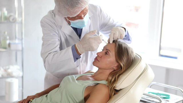 Middle-aged female patient lying on clinical chair undergoing face care procedure by injection method 