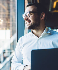 Content businessman standing beside window with laptop