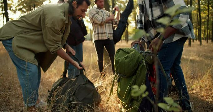A group of people in special hiking clothes pick up their hiking backpacks and begin to move through the sunny summer forest. The end of the camping trip and the beginning of a new path