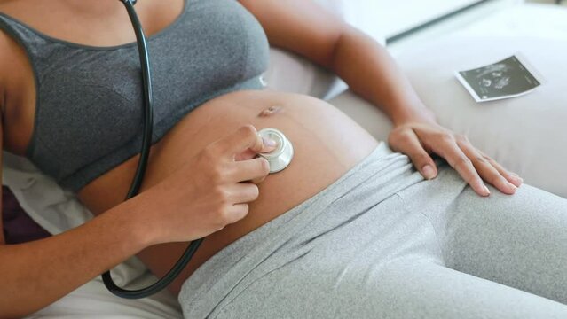 Pregnant Thai-African American mother happily uses medical stethoscope listen to the heartbeat of her fetus and excitedly placed the ultrasound images on the bed as the baby moved in the womb.