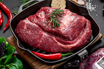 Raw organic marbled beef with spices on a wooden cutting board on a black slate, stone or concrete background.