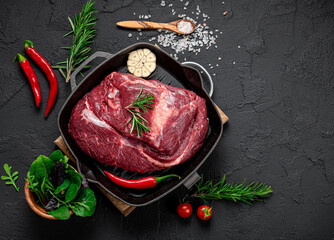 Raw organic marbled beef with spices on a wooden cutting board on a black slate, stone or concrete background.