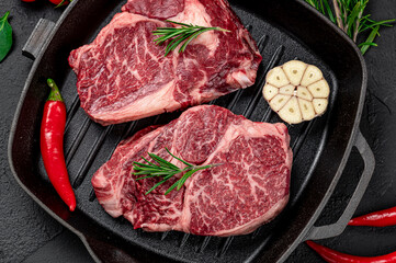 Raw organic marbled beef steaks with spices on a wooden cutting board on a black slate, stone or concrete background.