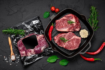 Raw organic marbled beef steaks with spices on a wooden cutting board on a black slate, stone or concrete background.