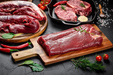 Raw organic marbled beef with spices on a wooden cutting board on a black slate, stone or concrete background.