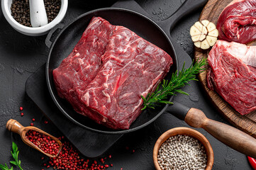 Raw organic marbled beef with spices on a wooden cutting board on a black slate, stone or concrete background.