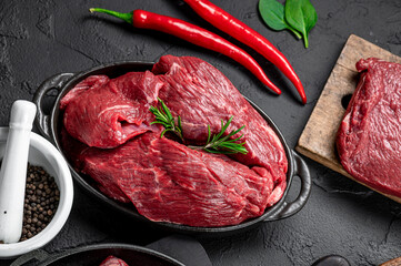 Raw organic marbled beef with spices on a wooden cutting board on a black slate, stone or concrete background.