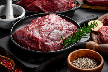 Raw organic marbled beef with spices on a wooden cutting board on a black slate, stone or concrete background.