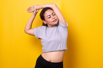 Fit young woman in sportswear stretching her arms over yellow background