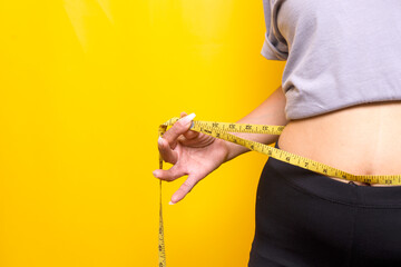Woman measuring her waist using tape over yellow background. Fitness and Sport Concept.