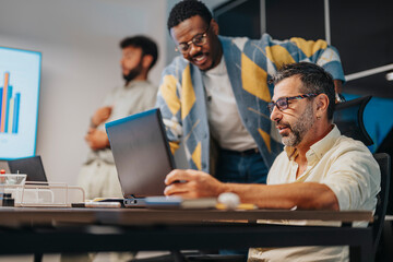 Multicultural business team collaborates in a board meeting. Professionals work together using technology to develop projects and achieve profit growth in a supportive and cooperative environment. - obrazy, fototapety, plakaty