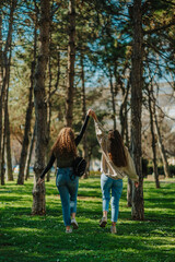 Fototapeta premium Female friends holding their hands up and hanging out in the park. Back view shot