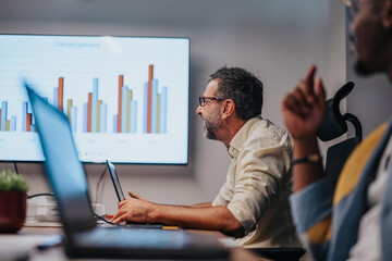 Multiracial business team discusses architectural blueprints, graph charts, and statistics in a modern office conference room, working together on a successful project.