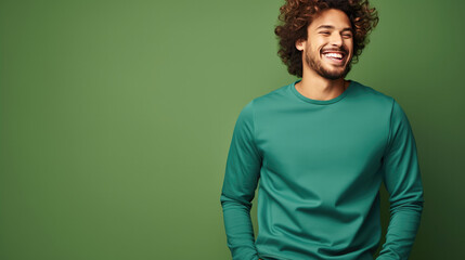 Fototapeta premium Ultra handsome man with curly hair, smiling and laughing, wearing a solid deep green sweatshirt. deep solid green background similar to the dress color.