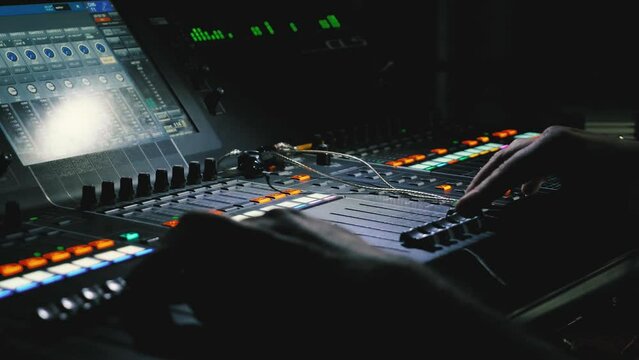 A sound engineer moves the levers of a multitrack mixing console. Close-up. Recording studio. Control parameters are displayed on the LED screen. The volume indicator tracks are running