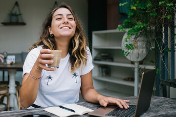 Happy woman enjoying coffee and using laptop