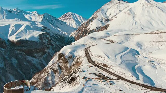 Aerial shot of snowy mountain and a road with cars. Sunny weather. Daytime