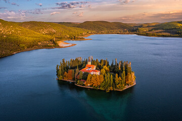 Visovac, Croatia - Aerial view of Visovac Christian monastery island in Krka National Park on a sunny autumn morning with golden sunrise, colorful autumn foliage and clear turquoise blue water