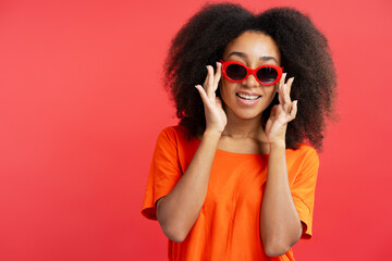 Positive attractive African American young woman with curly hair wearing stylish red sunglasses