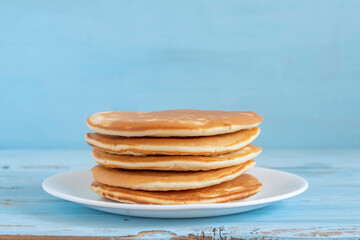 Stack of pancakes in ceramic plate over blue wooden background.

