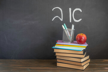 Stack of books and notebooks, red apple, pencil holder on wooden desk in front of blackboard with Hebrew letters "alef" and "bet". Back to school concept. - Powered by Adobe