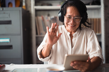 Smiling mature old woman holding using digital tablet sitting  while online video call with friend or relative cousin at home living room. Internet information technology and lifestyle concept.