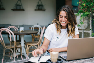 Young woman browsing internet and taking notes in cafe