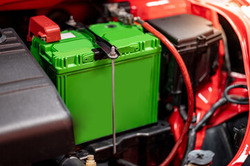 New green car battery installed near the car engine under the hood of red car in auto repair garage. Mechanical engineering and automotive industry concepts