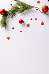 Vertical image of stars, baubles decorations and fir tree branch with copy space on white background
