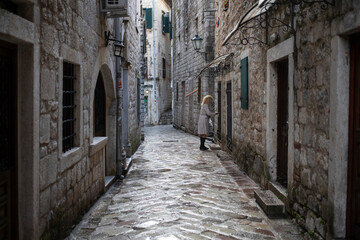 Fototapeta na wymiar Montenegro, Sep 15, 2023: A blonde woman wearing a raincoat leaves home in Kotor Old Town