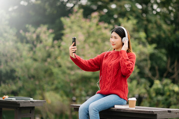 Fototapeta na wymiar Beautiful young asian woman listening to music with headphone with feeling happy and relaxed, fresh with smiley face. in the park