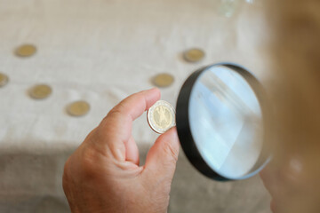 Woman with magnifying glass looking closely to 2 euro coins - obrazy, fototapety, plakaty