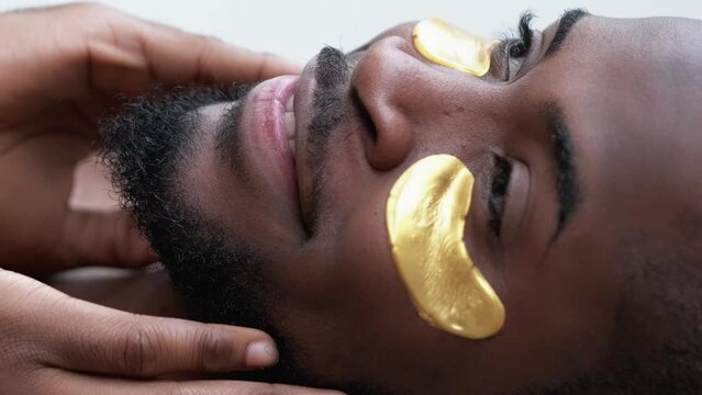 Vertical video. Facial treatment. Care ritual. Satisfied man with gold hydrogel skincare moisturizing eye patches touching perfect beard radiant face skin