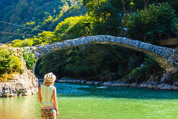 Adjara, Georgia.
Girl traveler enjoys scenic view of Queen Tamara Arch Bridge in Makhuntseti,...