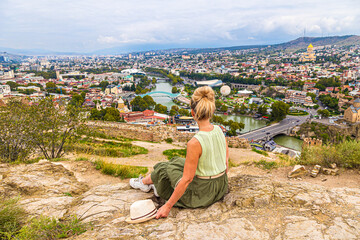 A girl tourist sitting on a hill enjoys a beautiful view of Tbilisi, Georgia.