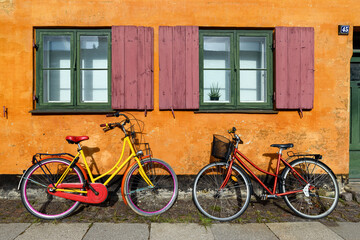 Bicycles in front of an orange house facace in Nyboder (historic row house district of former Naval barracks in Copenhagen, Denmark). - obrazy, fototapety, plakaty