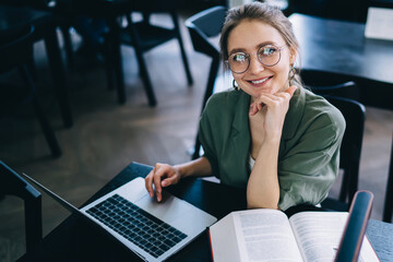 Smiling woman sitting at laptop and looking at camera while studying