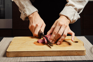 Unrecognizable woman slicing raw beef on cutting board