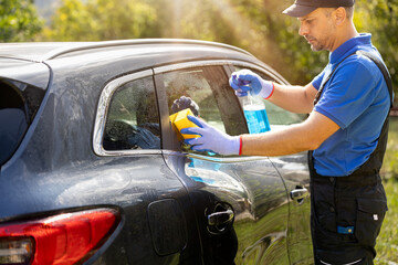 Car wash worker waxing windows by using spray bottle