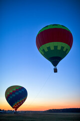 Colorful Air Balloons Levitating Over the Field Outdoors Against Clear Blue Skies At Twilight.