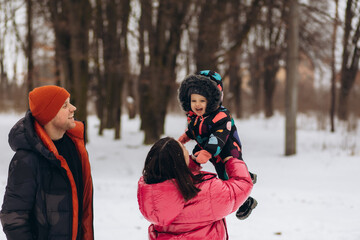 Young contemporary family of father, mother and son enjoying winter day in park while African American man carrying little boy on shoulders