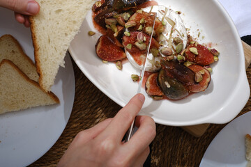 man eating melted brie cheese with figs and pistachios close-up of hands top view