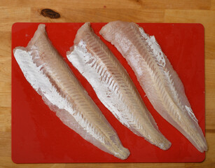 Filety rybne surowe leżą na plastikowej desce do krojenia