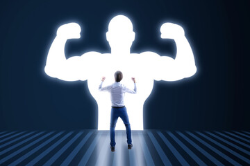 Back view of young businessman with very strong illuminated shadow flexing muscles on dark wall background. Personal development, inner strength, motivation concept.